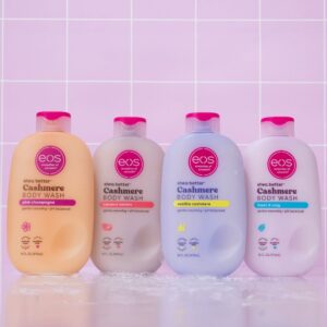 Four bottles of EOS Shea Better Cashmere Body Wash in Pink Champagne, Coconut Waters, Vanilla Cashmere, and Fresh & Cozy scents, displayed against a pink tiled background, showcasing their gentle, pH-balanced formulas for smooth, nourished skin.