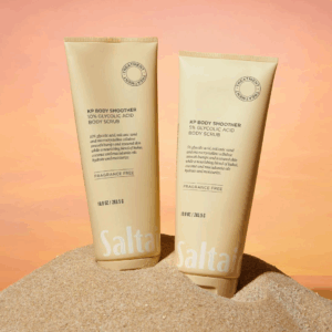 Saltair KP Body Smoother 5 percent and 10 percent Glycolic Acid Body Scrubs displayed upright on sand against a warm sunset background.