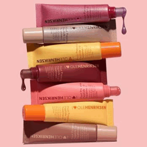 Flat lay of multiple Ole Henriksen Pout Preserve Lip Treatment tubes in assorted shades on a pink background.