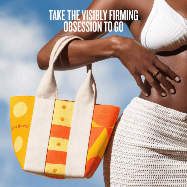 Model holding Sol de Janeiro mini canvas tote in orange and yellow under a bright blue sky
