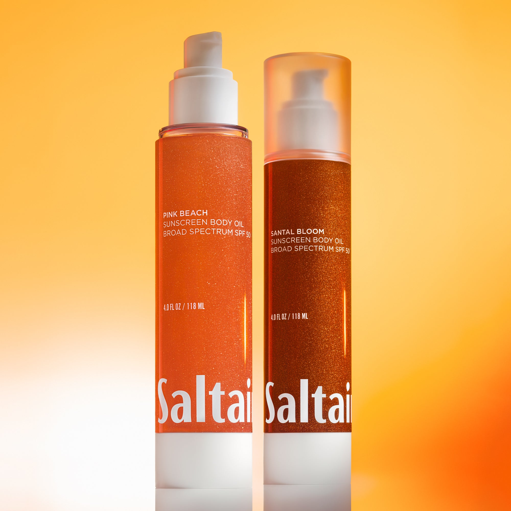 Saltair Pink Beach and Santal Bloom sunscreen body oil bottles standing side by side against warm gradient background